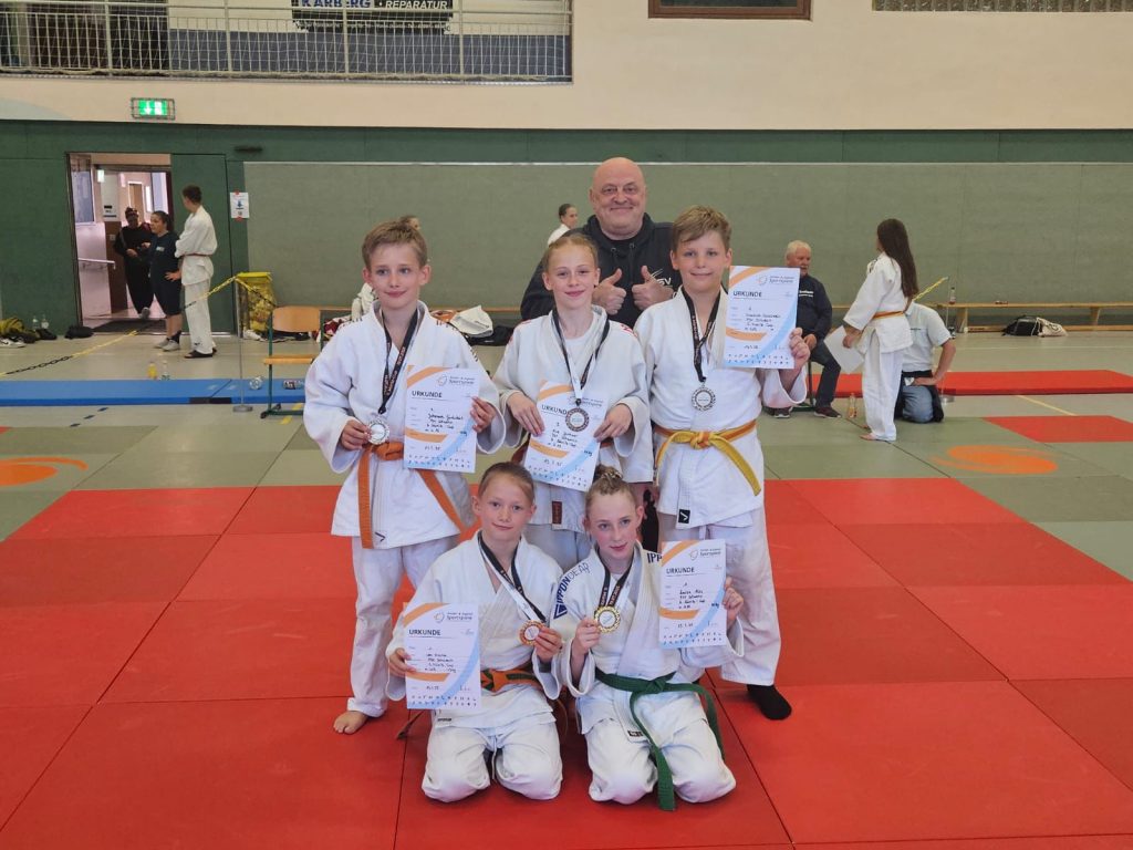 Die Judoka der U13 und U15 des PSV Schwerin posieren auf der Judomatte mit ihrem Trainer und ihren Medaillen nach dem erfolgreichen Wettkampf.